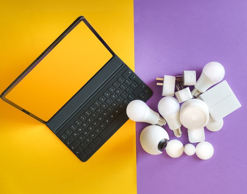 Flat lay of smart home gadgets and a keyboard on vibrant background depicting modern technology.