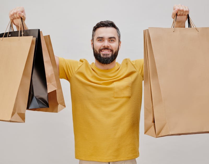 Man in a yellow shirt smiling and holding multiple shopping bags, representing gift options for men and high-tech gadgets.