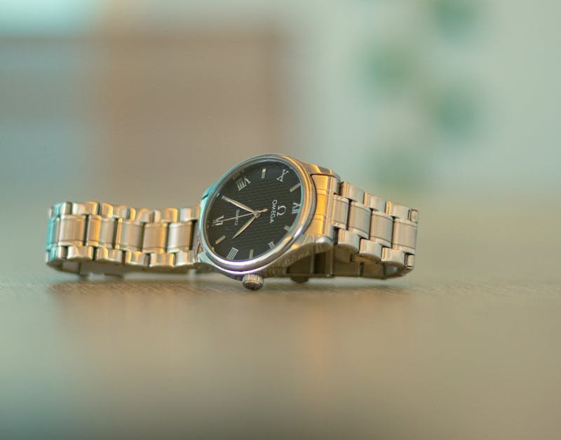 Omega wristwatch with a black dial and silver bracelet on a wooden surface, highlighting luxury and craftsmanship.