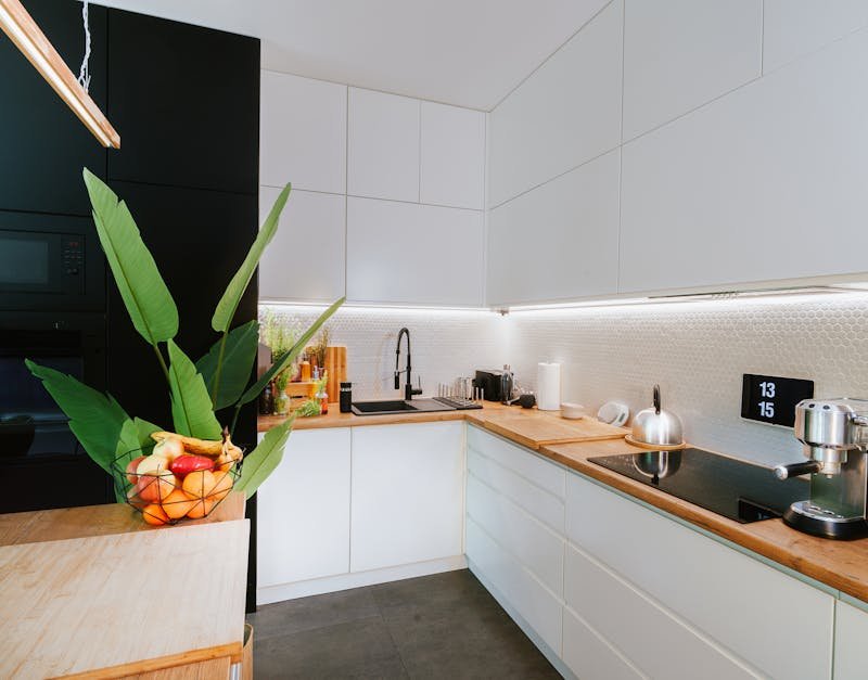 Modern kitchen featuring sleek cabinets, a wooden countertop, high-tech appliances, and a bowl of fresh fruits with greenery, illustrating high-tech home appliances and stylish design.