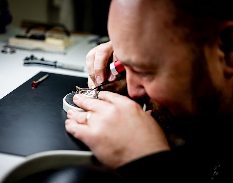 Watchmaker repairing a luxury Omega watch movement with precision tools on a workbench.
