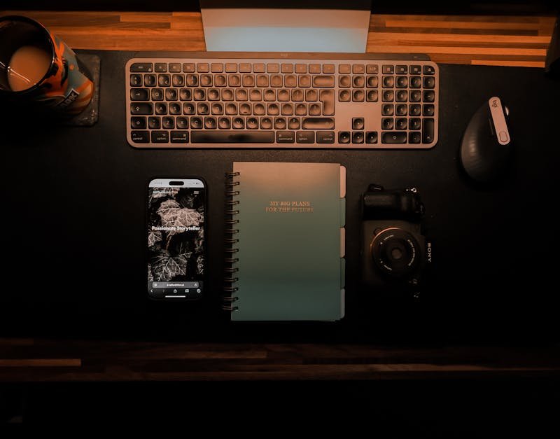 Top-down view of an organized desk setup featuring keyboard, camera, notebook, and smartphone for creative planning.