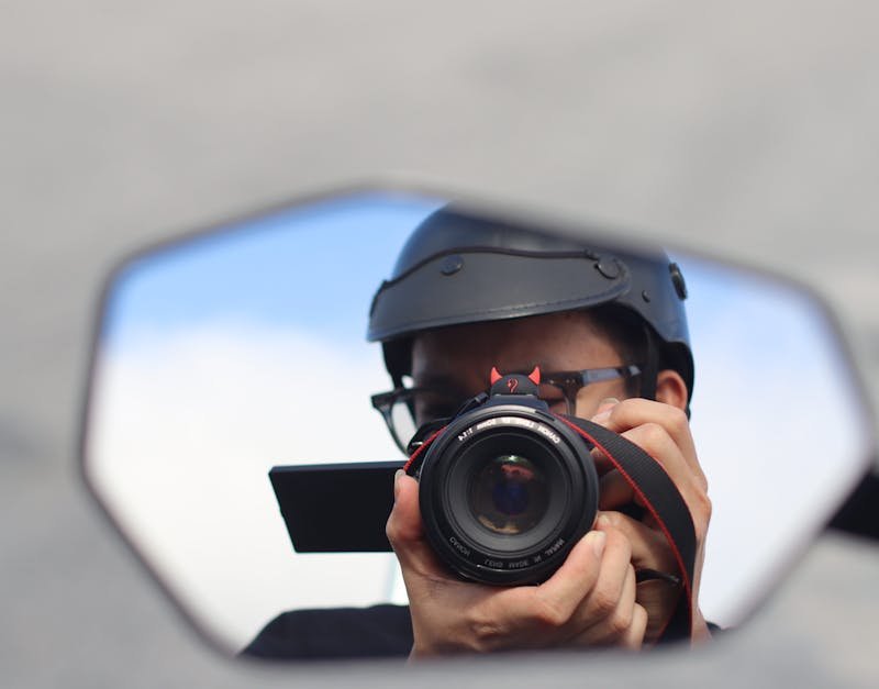 Person wearing a helmet taking a photo with a camera, reflecting in a mirror, emphasizing high-tech photography gear.