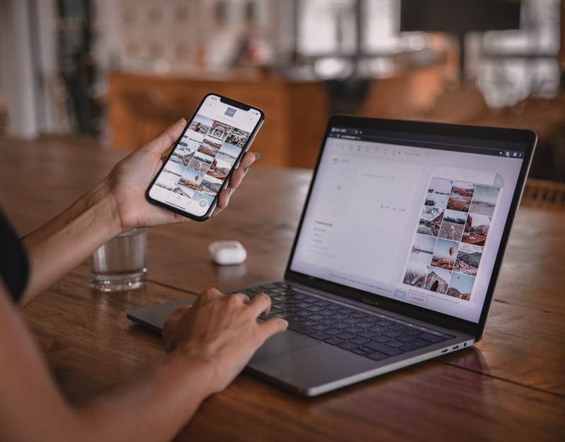 Person using smartphone and laptop for editing images, showcasing multitasking in a tech-savvy workspace.
