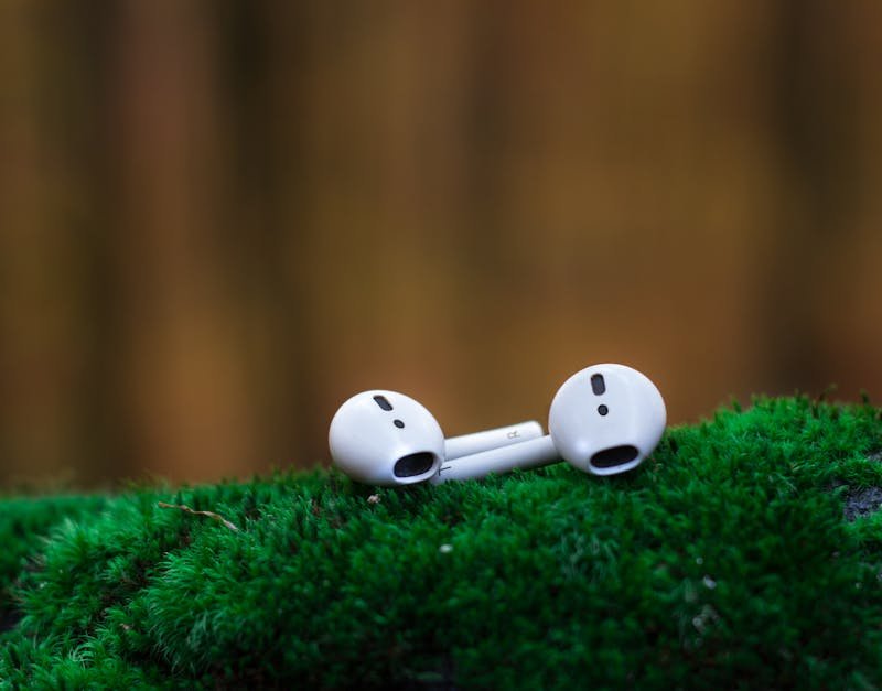 Close-up of wireless earbuds resting on vibrant green moss, showcasing portable audio technology.