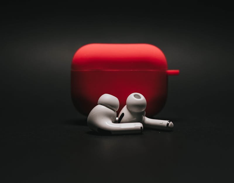 Sleek white earbuds with modern red case on a dark surface, highlighting stylish audio technology.