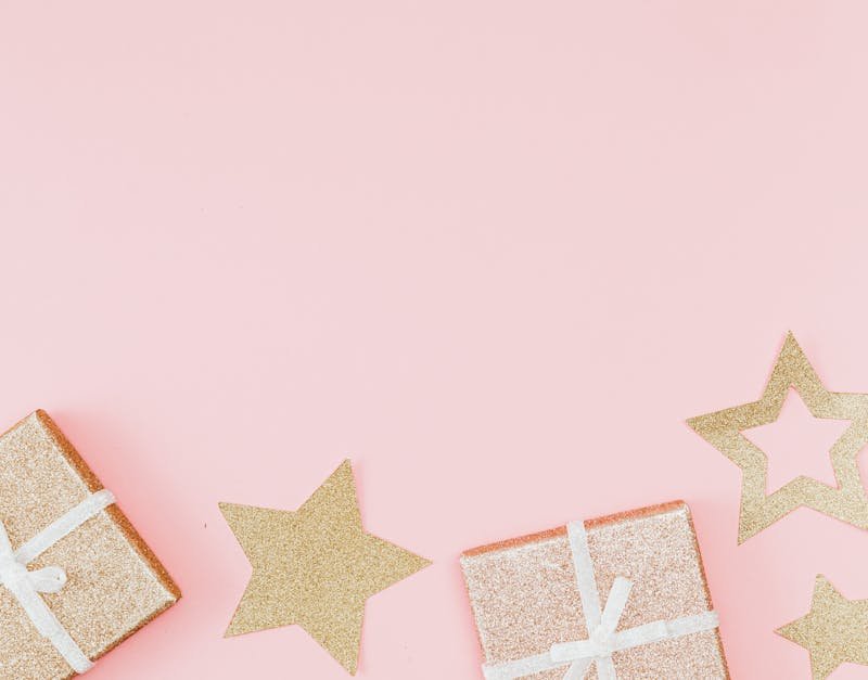 Glittery gift boxes with gold stars offer a festive and elegant scene against a soft pink background.