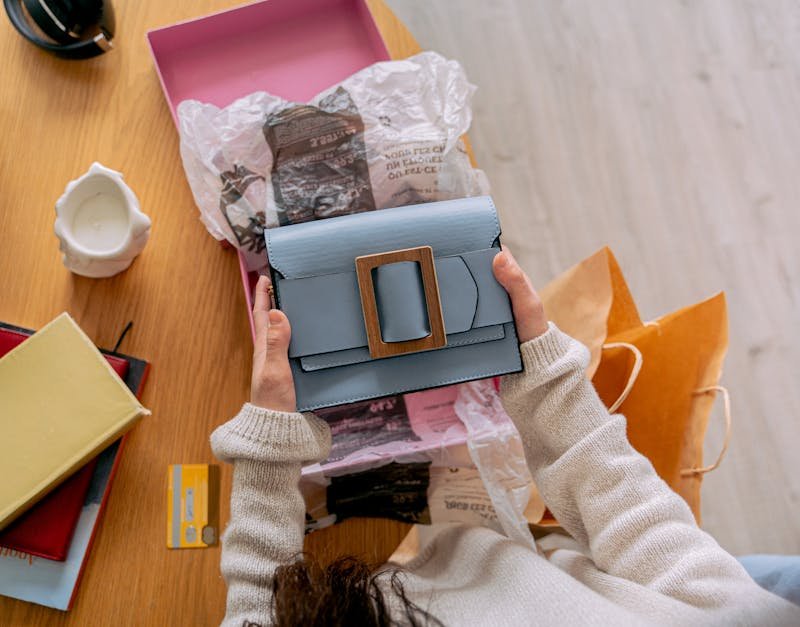 A person unboxes a chic blue handbag at home, surrounded by paper and shopping bags.