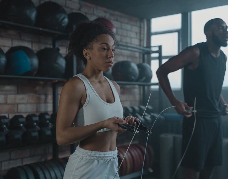 Woman holding jump rope in gym, preparing for workout, with fitness equipment in the background.