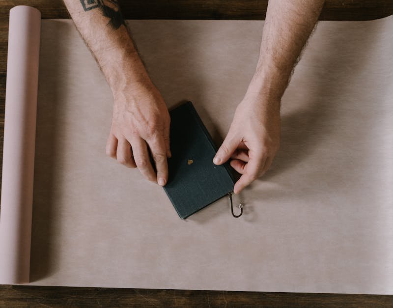Hands placing a green notebook on a brown surface with wrapping paper, relevant to smartphone review and buying guide context.