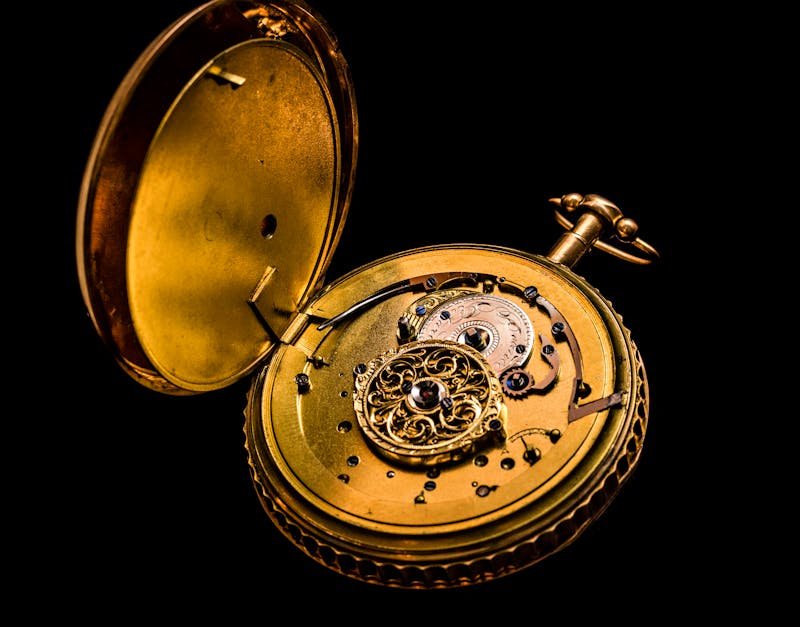 Detailed photograph of a vintage gold pocket watch showing intricate mechanics on a black background.