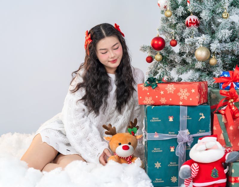 Young woman with holiday gifts and Christmas tree, embracing festive spirit.