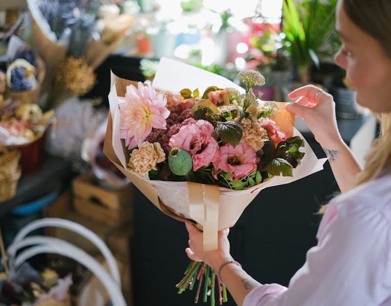 A woman holding a colorful flower bouquet in a cozy flower shop setting.