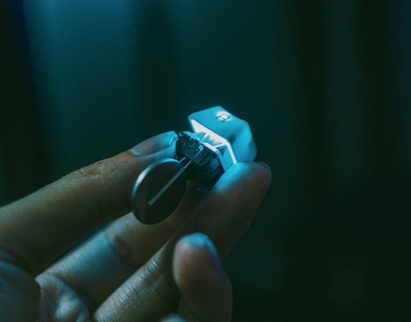 A close-up view of a hand holding a mechanical keyboard switch with a keycap attached.