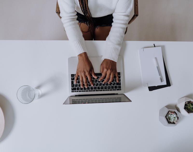 Top view of a woman typing on a laptop at a modern, minimalist home office desk with plants.