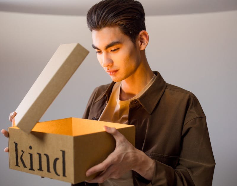 A man opens a cardboard box labeled 'kind' revealing a bright glow inside.