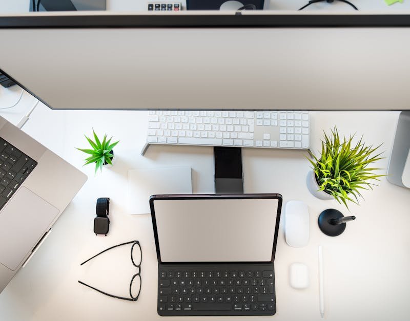 Top view of a minimalist workspace setup with laptop, tablet, and greenery.