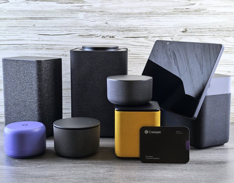A collection of various smart home speakers and tablet displayed on a wooden surface.