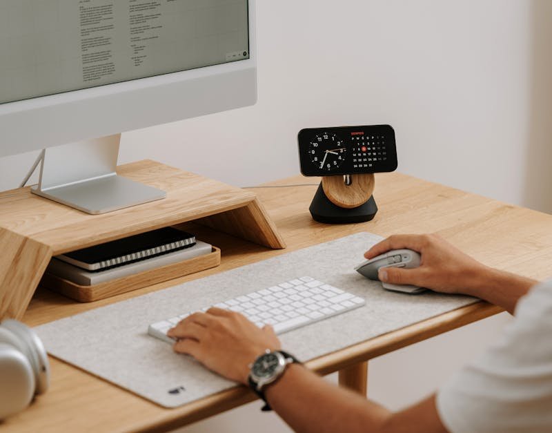 A clean and modern desk setup featuring a computer, clock, and accessories in a home office.