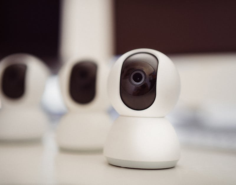 Close-up of three smart home security cameras placed on a white desk indoors.