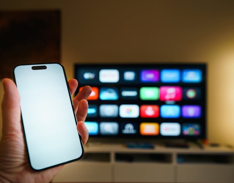 A smartphone in focus with a smart TV displaying apps in a cozy living room.